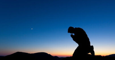 Man praying on the summit of a mountain at sun set with the moon in the sky.