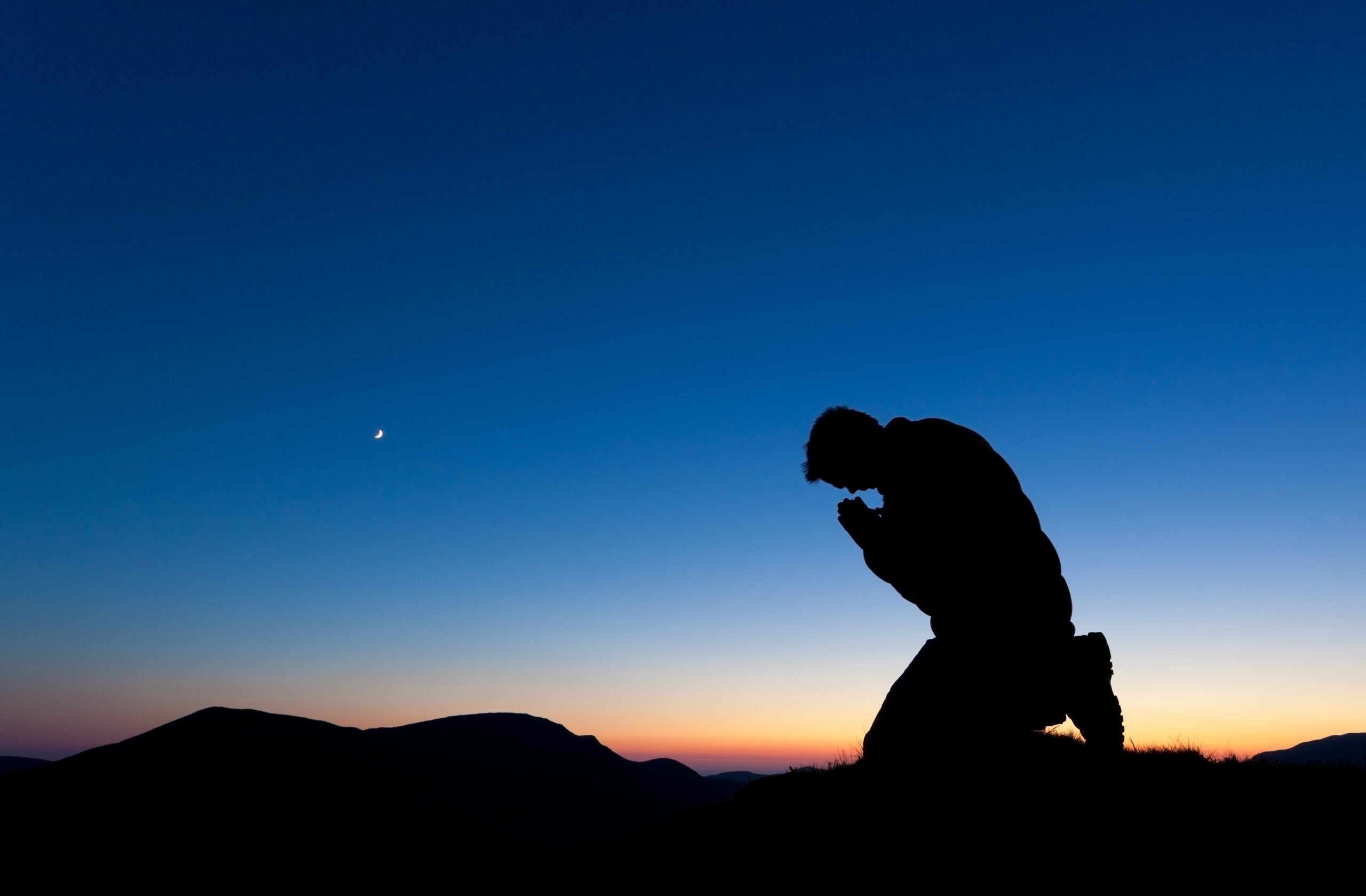 Man praying on the summit of a mountain at sun set with the moon in the sky.